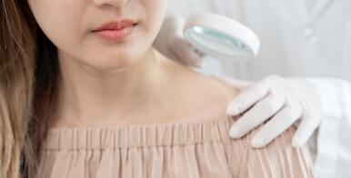 A dermatologist uses a magnifying glass on a patient's skin.